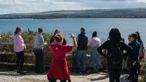 A group being given a talk whilst looking out to sea.
